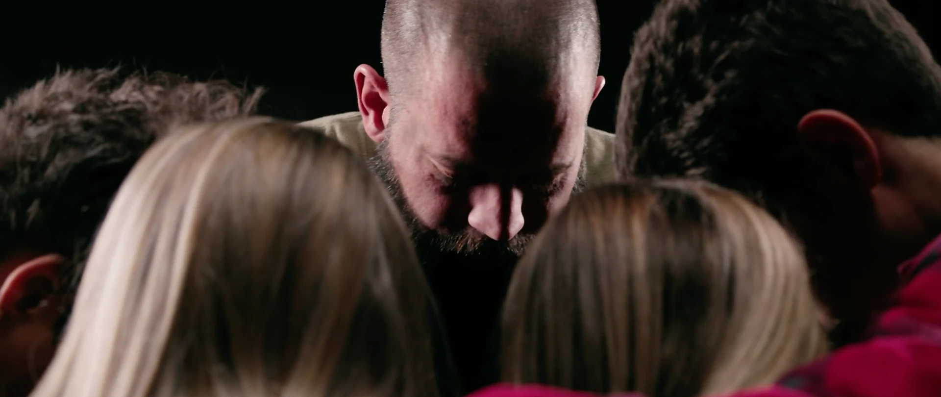 Jeff Marr with his head bowed in a tight huddle with his family