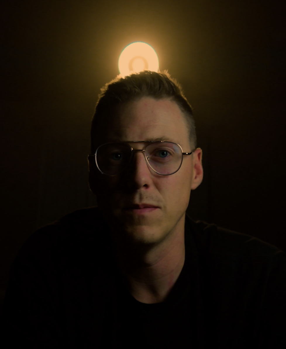 Portrait of filmmaker James Merkley lit by a single warm light